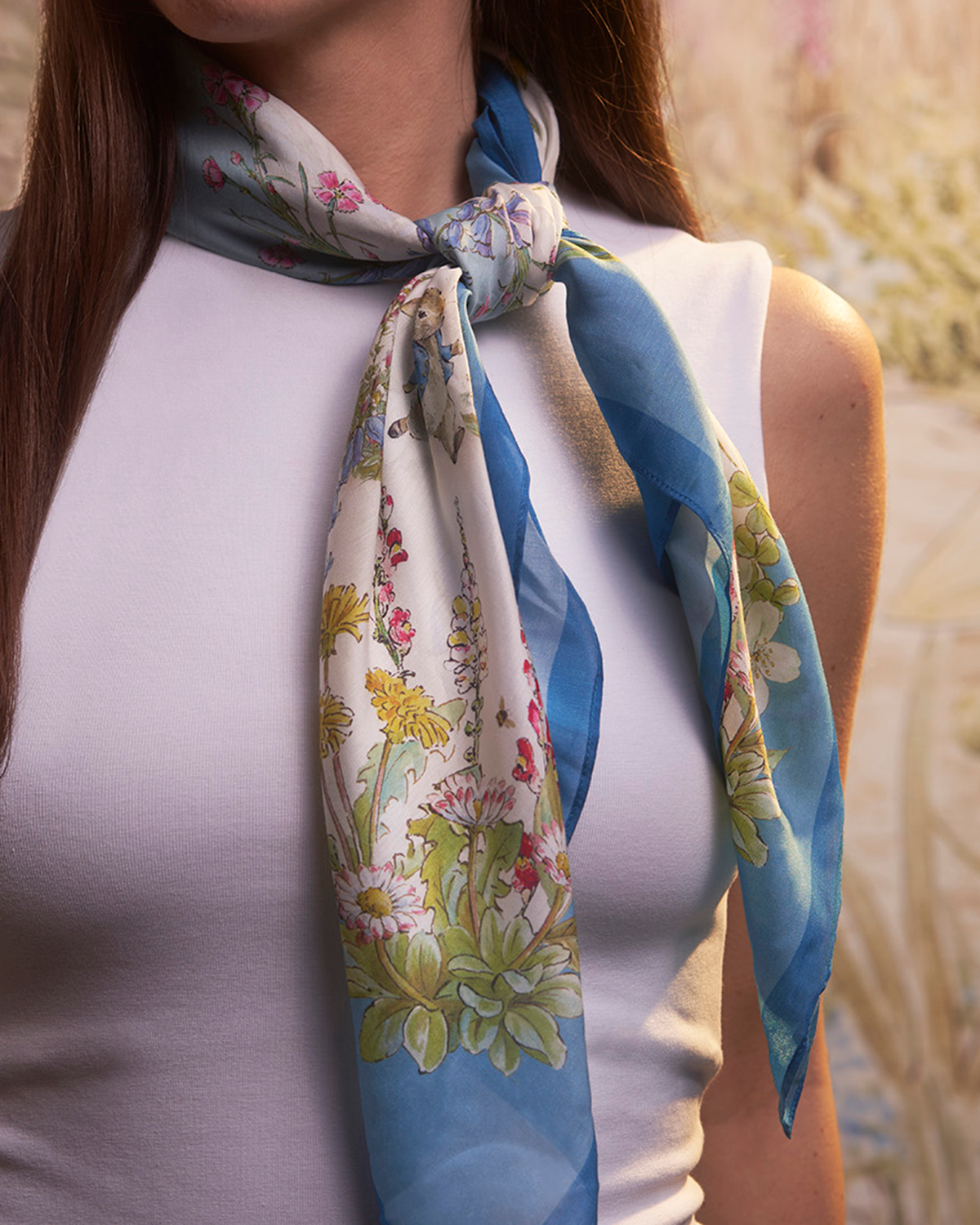 Woman wearing a cream and blue floral scarf with a blurred natural background