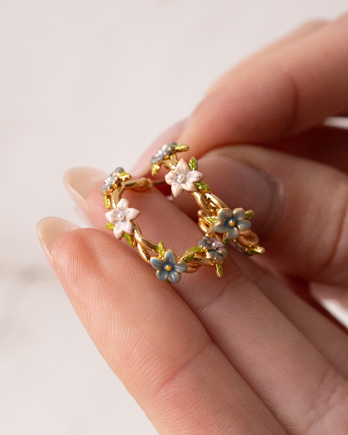 Gold hoop earrings with floral designs held between fingers on a light background